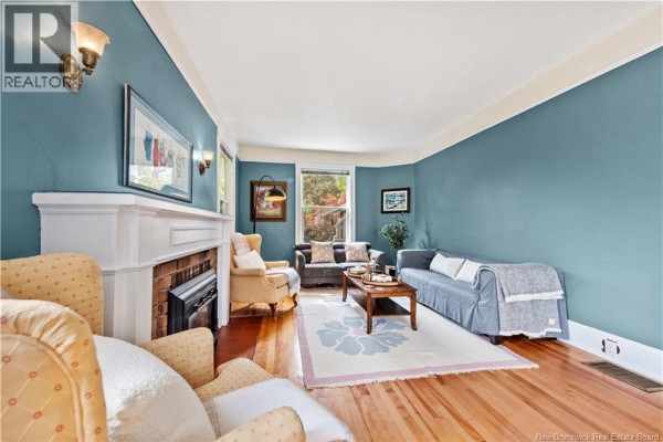 Living room with blue walls, a white fireplace, hardwood floors, and a bay window with seating. - 248 Highfield Street, Moncton