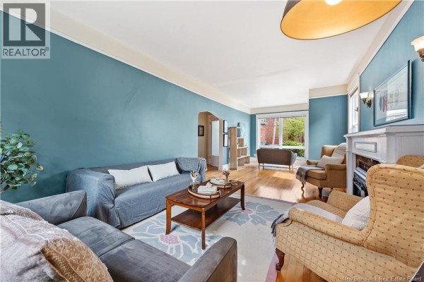 Spacious living room with blue walls, hardwood floors, fireplace, and multiple seating arrangements. - 248 Highfield Street, Moncton