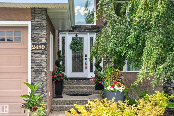 Close-up of the front entrance with a white door, stone accents, and potted plants. - 2489 Martell Cr Nw Nw, Edmonton