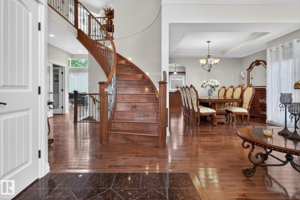 View of the foyer with a curved wooden staircase, gleaming hardwood floors, and a dining room. - 2489 Martell Cr Nw Nw, Edmonton