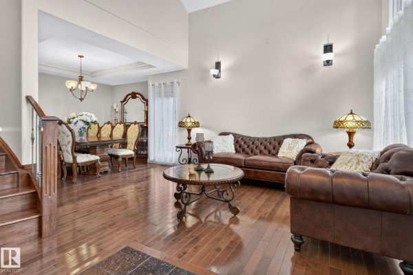 Spacious living room featuring a large brown leather sofa, wooden floors, and a formal dining area. - 2489 Martell Cr Nw Nw, Edmonton