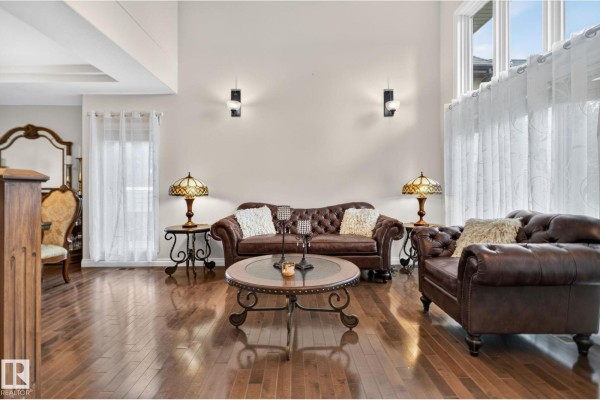 Living room with a tufted leather sofa, decorative lamps, round coffee table, and tall windows. - 2489 Martell Cr Nw Nw, Edmonton