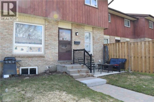 Side view of the townhouse exterior showing the brick and wood facade and fenced yard. - 249 Cedarbrae Avenue Unit# 1, Waterloo
