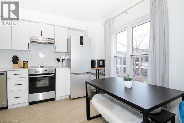 Apartment kitchen with white cabinets, stainless steel appliances, and a dining table. - 249 Emerald Street N Unit# 2, Hamilton