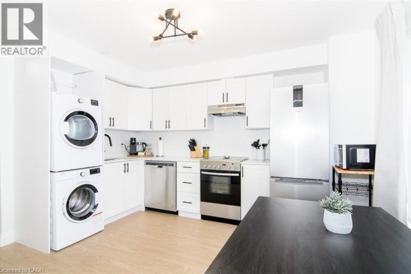 Apartment kitchen with white cabinets, stacked washer and dryer, and stainless steel appliances. - 249 Emerald Street N Unit# 2, Hamilton