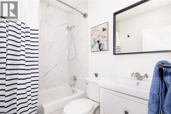 Apartment bathroom with a white tub, white vanity, and a black and white striped shower curtain. - 249 Emerald Street N Unit# 2, Hamilton