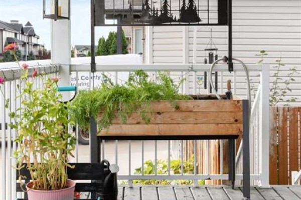 A wooden planter box filled with greenery sits on a covered porch with white railings. - 249 Somerset Way Se, Medicine Hat