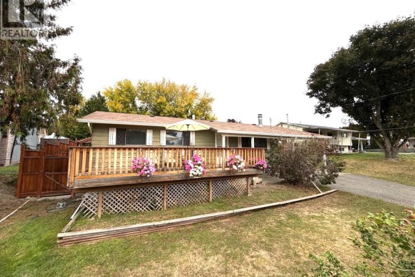 Exterior view of a house with a wooden deck, grass lawn, and trees. - 2490 Smid Road, West Kelowna