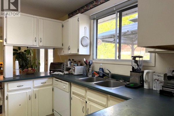 Kitchen with white cabinets, dark countertops, and a double sink looking out a window. - 2490 Smid Road, West Kelowna