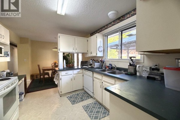 Kitchen with white cabinets, appliances, and a view of a dining area through an opening. - 2490 Smid Road, West Kelowna