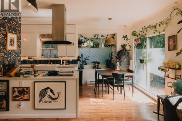 Kitchen with white cabinets, island, dark floral wallpaper, and dining area. - 25 5988 Hastings Street, Burnaby