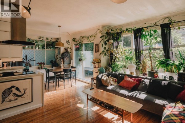 Open concept living and dining area with large sofa, coffee table, and plants. - 25 5988 Hastings Street, Burnaby
