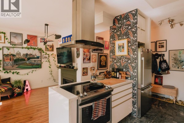 Kitchen island with stovetop, refrigerator, and patterned wallpaper accent wall. - 25 5988 Hastings Street, Burnaby