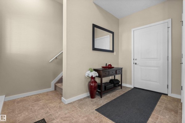 Entryway with a white door, a console table, mirror, and tiled floor. - #25 655 Watt Blvd Sw, Edmonton