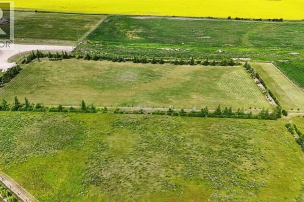 Overhead view of a spacious, fenced green field with a backdrop of yellow farmland under a blue sky. - 25 713019 Rge Rd 71, Rural Grande Prairie No  1, County Of