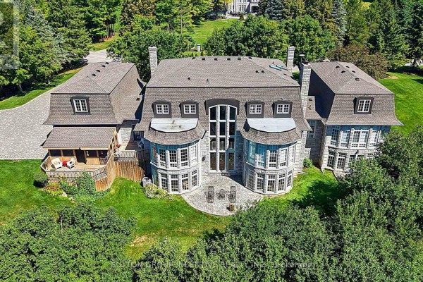 Rear view of a stone mansion with multiple bay windows and a wooden deck. - 25 Bovair Trail, Aurora