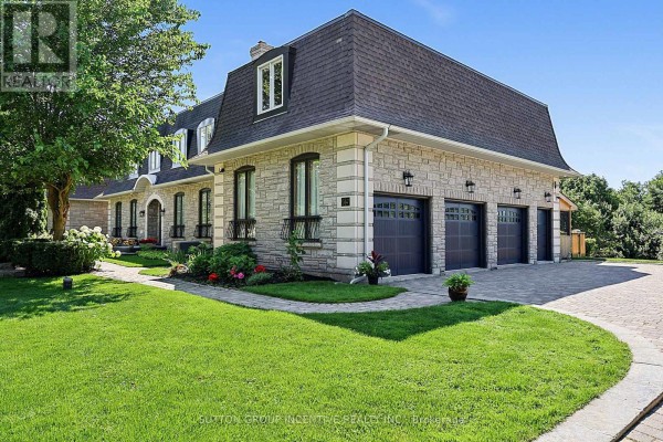 Side view of the house showcasing a stone facade, mansard roof, and three garage doors. - 25 Bovair Trail, Aurora