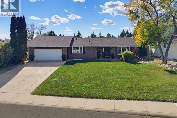 Front exterior of a single-story brick house with a manicured lawn and double garage. - 25 Capilano Drive, Saskatoon