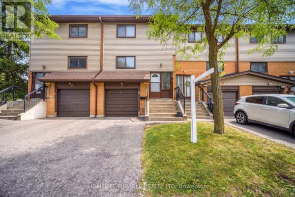 Front view of a townhouse with beige siding, brick accents, and two garage doors. - 25 Carleton Place, Brampton