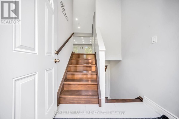 Interior view of townhouse entrance with white door, hardwood stairs, and light gray walls. - 25 Carleton Place, Brampton