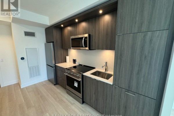 Galley kitchen with dark gray cabinetry, stainless steel appliances, and light laminate flooring. - 25 Cordova Avenue, Toronto