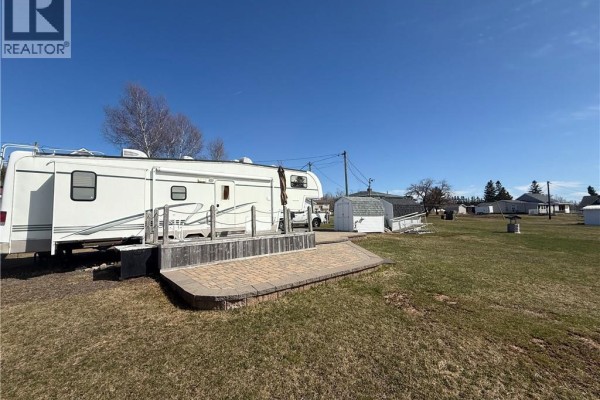White recreational vehicle with attached wooden deck and patio in a grassy yard. - 25 Cottage Lane, Cocagne