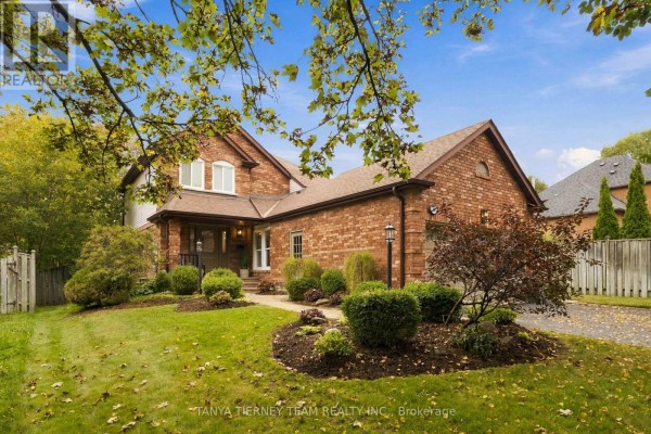 Side view of a brick house with manicured shrubs, a paved driveway, and a wooden fence. - 25 Coulton Court, Whitby