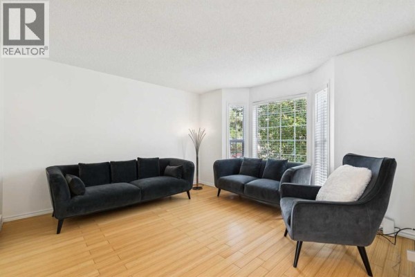 Living room with light wood floors, white walls, a bay window, and dark grey sofas. - 25 Coville Gardens Ne, Calgary