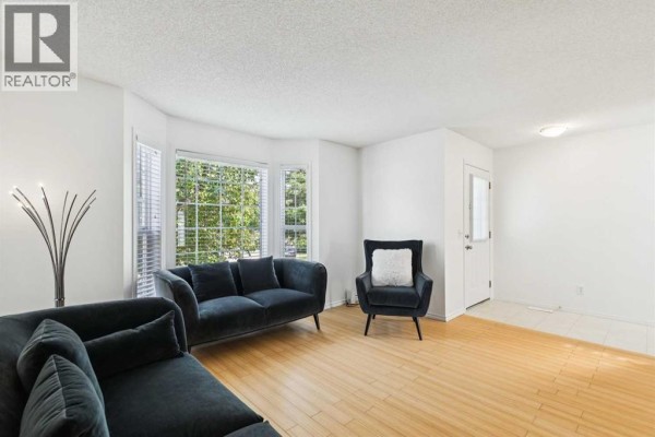 Living room with light wood floors, white walls, a bay window, and dark grey seating. - 25 Coville Gardens Ne, Calgary