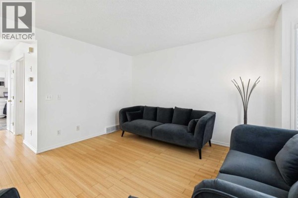 Living room with light wood floors and white walls, featuring a dark grey sofa and armchair. - 25 Coville Gardens Ne, Calgary