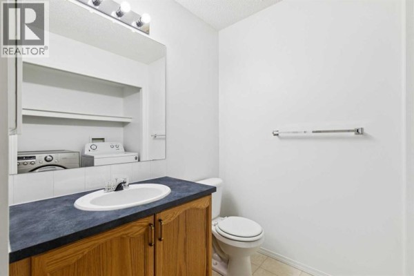 Bathroom with a vanity, sink, toilet, and stacked washing machine and dryer in the corner. - 25 Coville Gardens Ne, Calgary