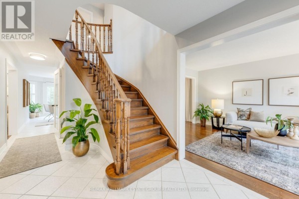 Interior view of a foyer with a wooden staircase, tiled floor, and living room access. - 25 Dewbourne Place, Whitby