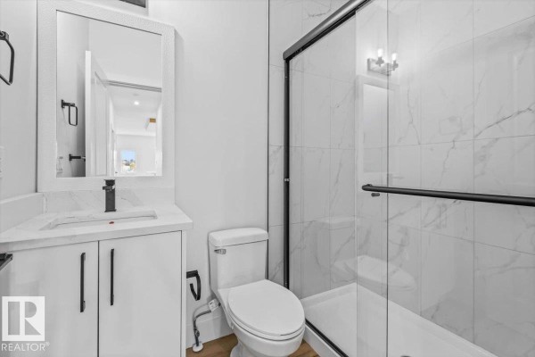 Bathroom with a white vanity, black faucet, toilet, and a glass-enclosed shower. - 25 Foxtail Rd, Fort Saskatchewan