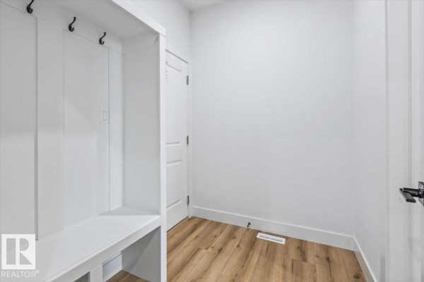 Mudroom with white built-in bench seating, coat hooks, and wood-look flooring. - 25 Foxtail Rd, Fort Saskatchewan
