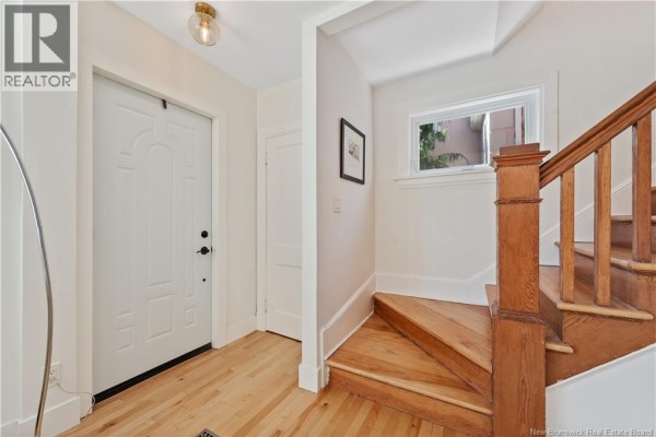 Interior entryway with a white door, wooden floor, and wooden staircase. - 25 Hillcrest Drive, Moncton