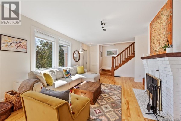 Living room with a fireplace, sectional sofa, a yellow armchair, and a wooden staircase in the background. - 25 Hillcrest Drive, Moncton
