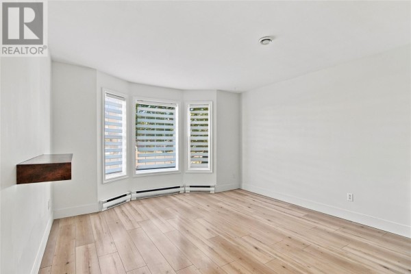 Empty room with light wood floors, white walls, and a bay window with blinds. - 25 Laumann Place, Mount Pearl