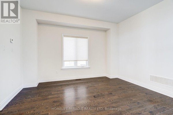 Empty room with dark hardwood floors and a white roller blind covering the window. - 25 Lorne Thomas Place, New Tecumseth