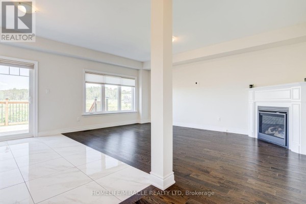 Living area with a fireplace, dark hardwood floors, and large windows overlooking a balcony. - 25 Lorne Thomas Place, New Tecumseth