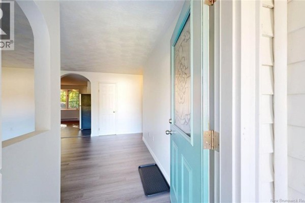 Interior view of the entryway showing the turquoise front door, white walls, and wood-look flooring. - 25 Mccarron Drive, Quispamsis