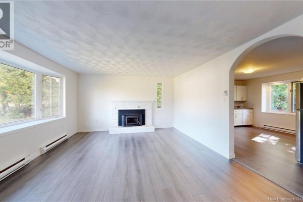 Living room with a fireplace, white brick hearth, large bay window, and archway to the kitchen. - 25 Mccarron Drive, Quispamsis