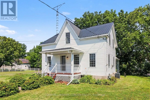 Side view of a white vinyl-sided house with a black metal roof, set against green trees. - 25 Mill Street, North Dundas