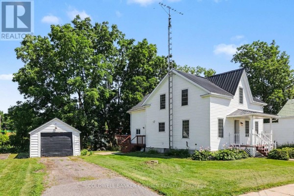 Rear three-quarter view of a white house with a detached garage and a large transmission tower. - 25 Mill Street, North Dundas