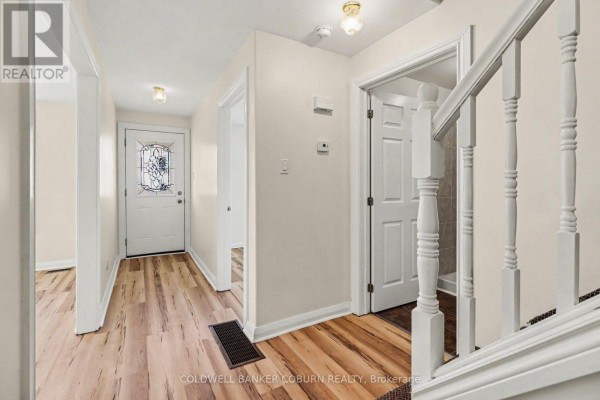 Interior hallway with light wood laminate flooring, a white staircase, and a glass-panelled front door. - 25 Mill Street, North Dundas