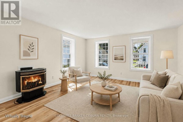 Living room with light wood floors, a sofa, chairs, a round coffee table, and a gas fireplace. - 25 Mill Street, North Dundas