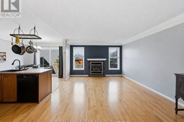 Living room with hardwood floors, a stone fireplace, and an open view to the kitchen area. - 25 Oldfield Street, Ottawa