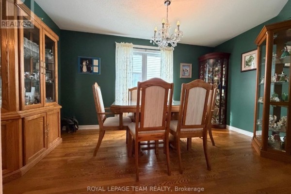 Formal dining room with a wooden table and chairs, glass display cabinets, and dark green walls. - 25 Redpath Drive, Ottawa