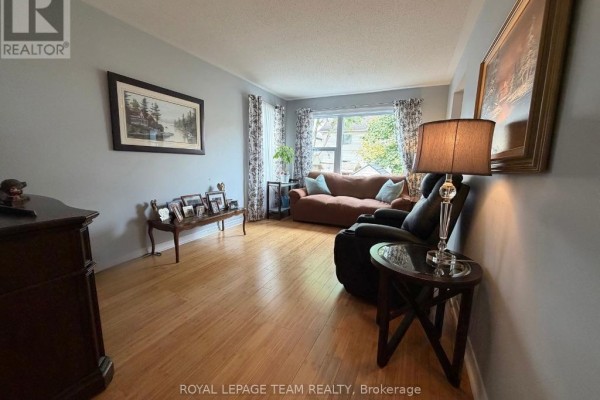 Living room with light blue walls, hardwood floors, a sofa, armchair, and a coffee table. - 25 Redpath Drive, Ottawa