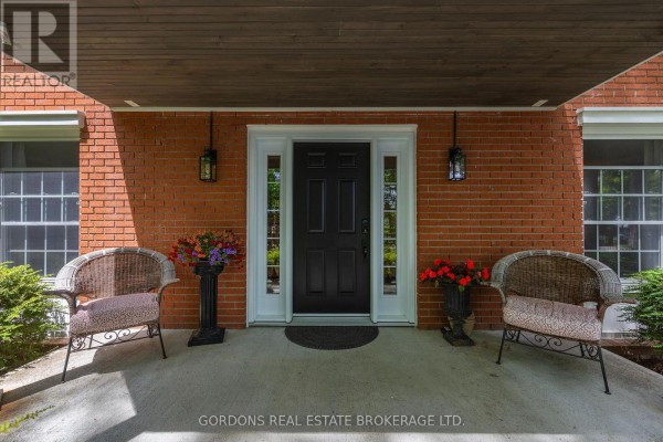 Covered front porch with two wicker chairs, planters, and a dark front door with sidelights. - 25 Riverside Drive, Kingston)