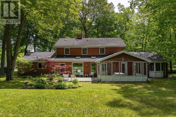 Rear exterior of a red brick house with a wooden deck, screened-in porch, and lush green backyard. - 25 Riverside Drive, Kingston)